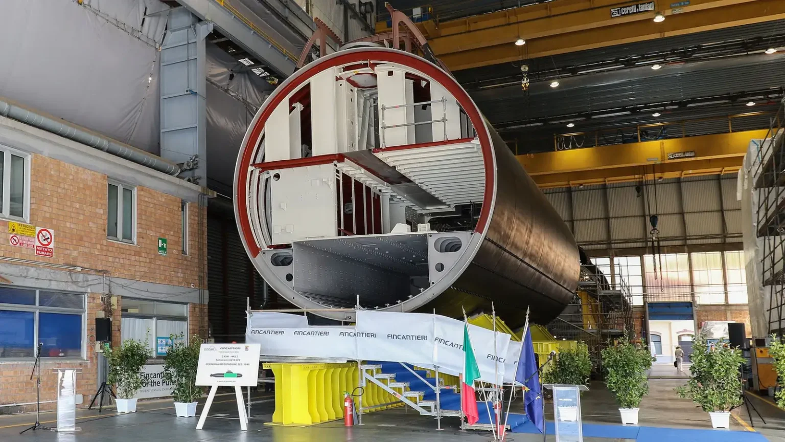 Τμήμα κελύφους υποβρυχίου U212NFS σε υπόστεγο του ναυπηγείου της Fincantieri στο Μουτζιάνο, με την ιταλική και την ευρωπαϊκή σημαία μπροστά του