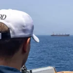 Ναύτης του αμερικανικού Ναυτικού, με την πλάτη στον φακό, παρατηρεί εμπορικό πλοίο στον ορίζοντα