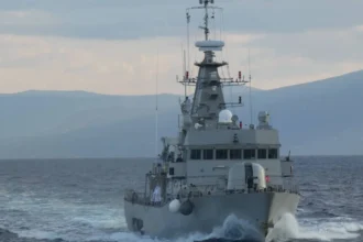 Γκρίζα κανονιοφόρος του Πολεμικού Ναυτικού πλέει κατά μέτωπο με ταχύτητα, με βουνά στο βάθος