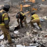 Διασώστες με κράνη ψάχνουν στα συντρίμμια κτιρίου στη Ζαπορίζια, με εκσκαφέα στο βάθος